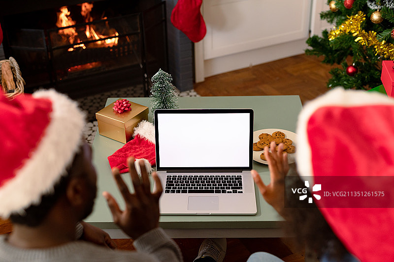非裔美国人夫妇戴着圣诞帽，使用带屏幕复制空间的笔记本电脑的背影图片素材