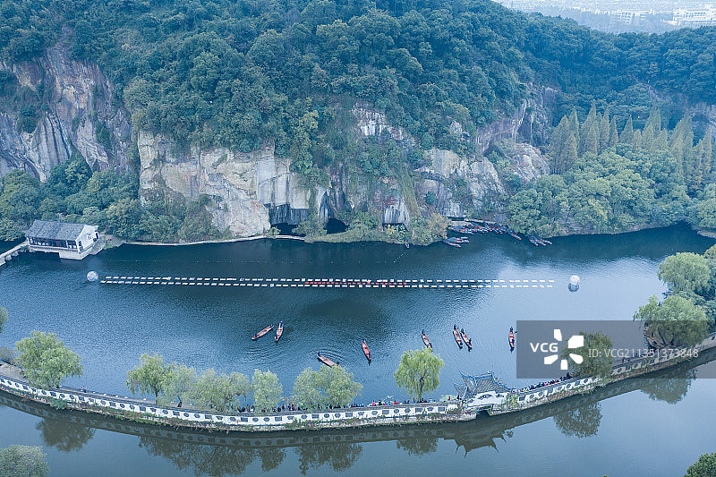 高视角航拍浙江绍兴岩石山体下有小船中式白墙建筑长廊的蓝色湖泊图片素材