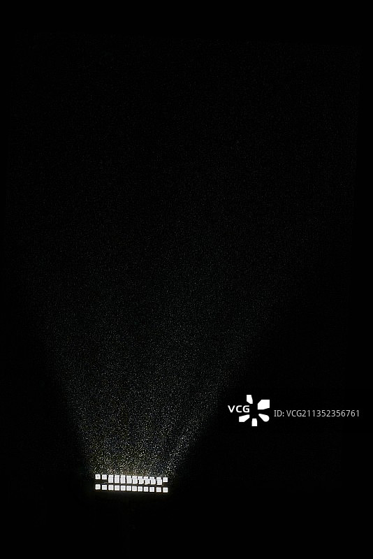 黑色背景下照明设备的光束照亮雨滴图片素材
