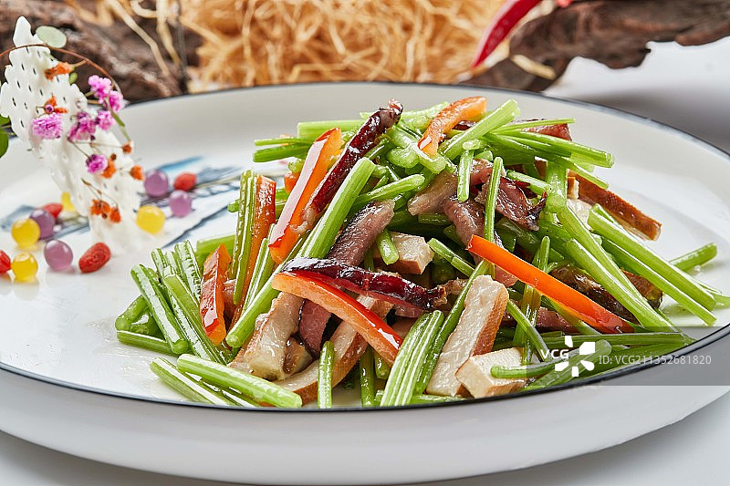 白色瓷盘装的腊肉彩椒茼蒿炒熏干子图片素材