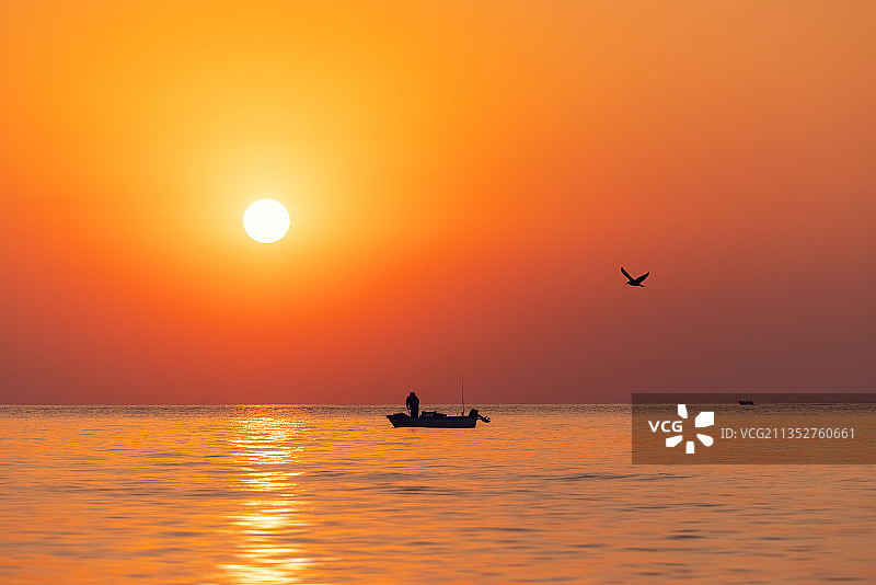 橙色天空下飞越海面的鸟群剪影图片素材