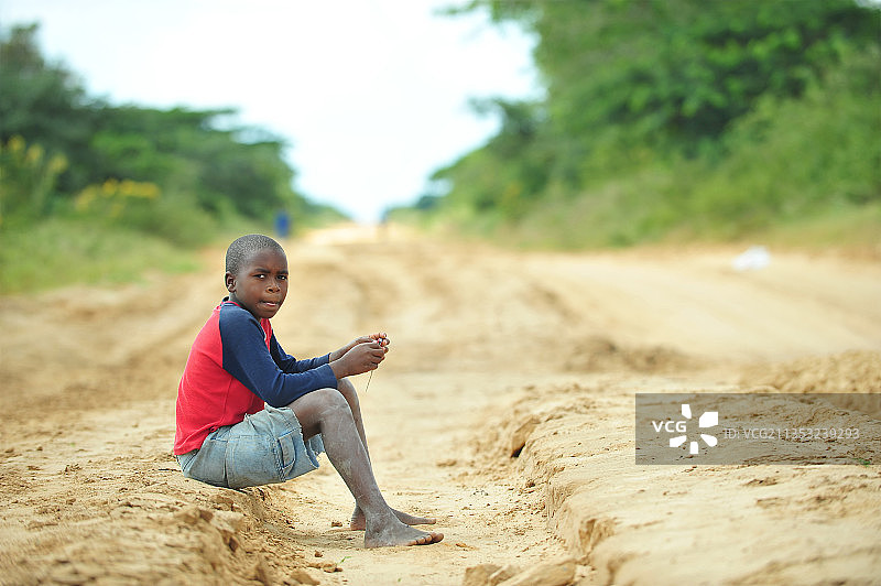 坐在土路上的男孩全身照，莫桑比克图片素材