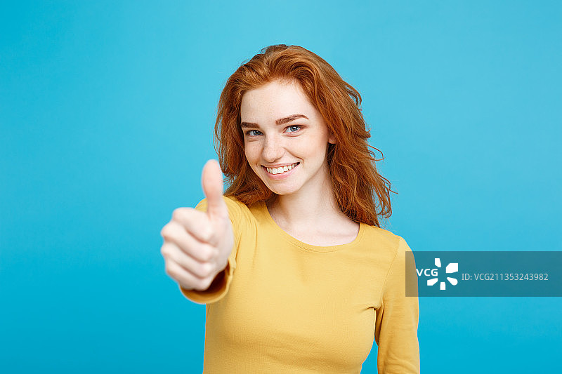在蓝色背景下，微笑的年轻女子做出竖起大拇指的姿势图片素材
