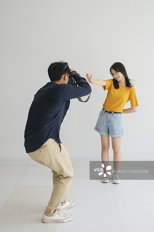 男摄影师在工作室里用白色的背景拍了一张十几岁模特女孩的照片。图片素材