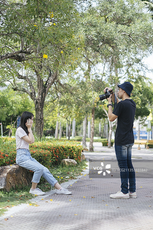 男摄影师给坐在伊佐拉丛林岩石上的模特女孩拍照。图片素材