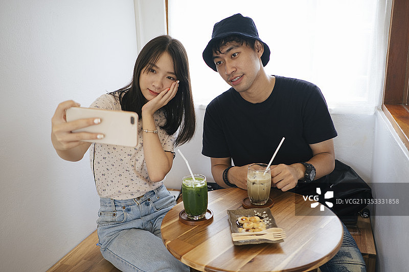 男人和女人在咖啡馆里一起自拍，桌上放着饮料和零食。图片素材