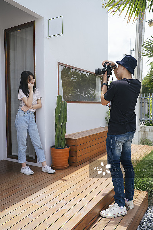 男摄影师在铺着仙人掌和木地板的咖啡馆前拍了一张十几岁模特女孩的照片。图片素材