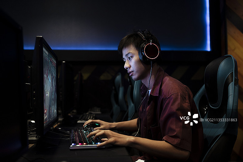 专业玩家在网吧玩电脑游戏，戴着耳机。和他的队友在电脑上聊天。图片素材