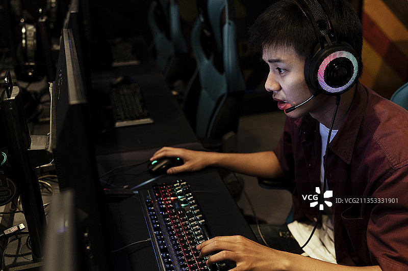 严肃的年轻亚洲玩家在网吧玩电脑游戏，戴着耳机，与朋友聊天。图片素材