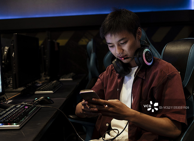 亚洲玩家与他的朋友在智能手机聊天，坐在网吧。图片素材