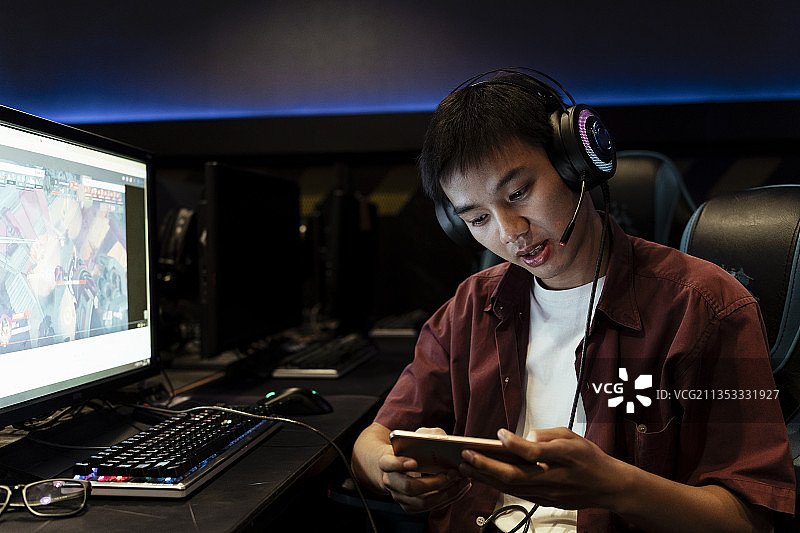 亚洲玩家玩手机游戏，戴着耳机，坐在网吧。图片素材