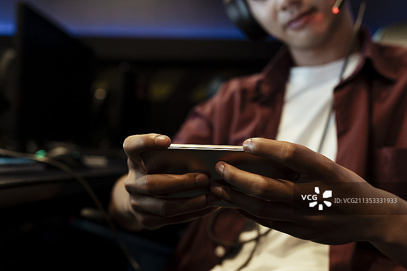 近手的亚洲玩家玩手机游戏与智能手机。图片素材