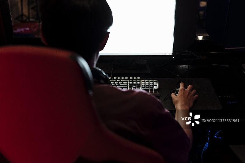 网吧的显示屏上有白屏。亚洲玩家坐在红色的椅子上玩电脑游戏。游戏上瘾。图片素材