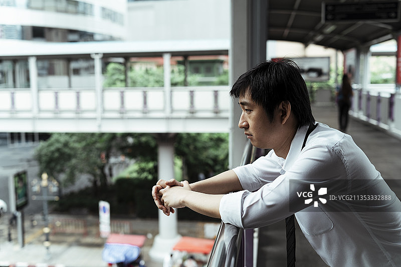 悲伤的商人靠在天桥的扶手上。绝望的商人看着立交桥下面的路。深思熟虑的商人思考他辞去工作后的生活。图片素材