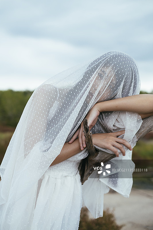 近距离-年轻的亚洲长发女子新娘与白色面纱倚靠在干燥的树户外肖像。图片素材