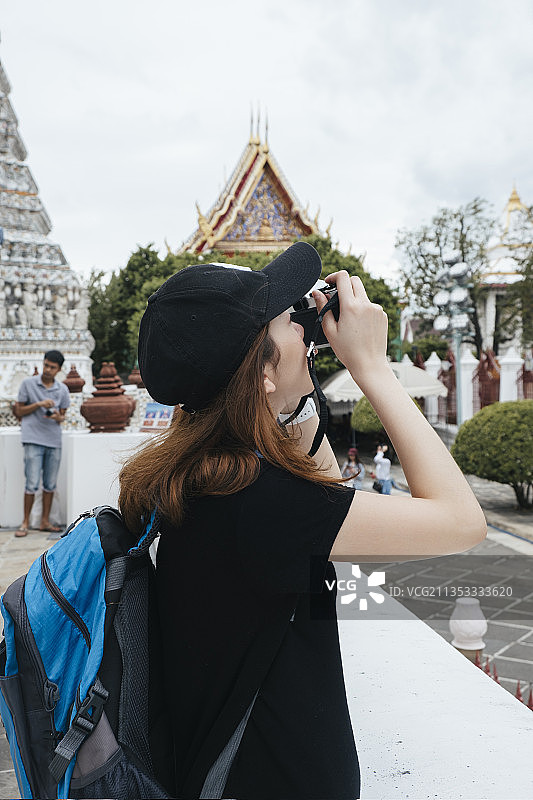 亚洲背包客女子在wat arun用相机拍照的侧视图。图片素材