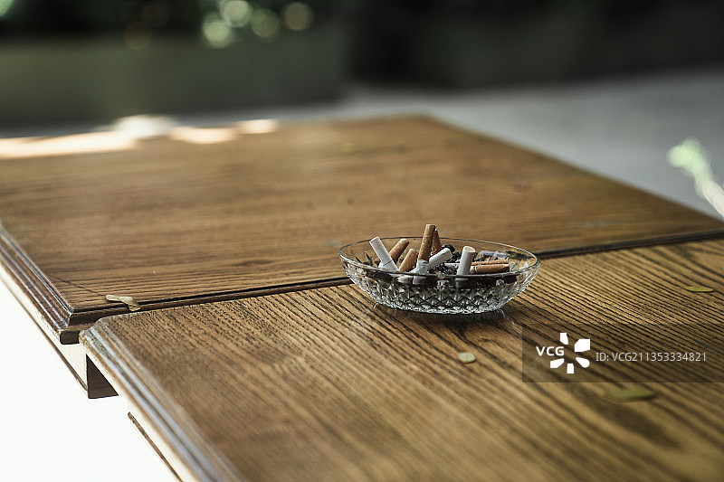 木桌上的玻璃烟灰缸里有许多烟头和烟灰。吸烟对身体不好。图片素材