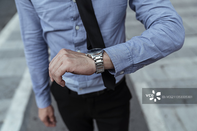商人看着手上的表，看着时钟。图片素材