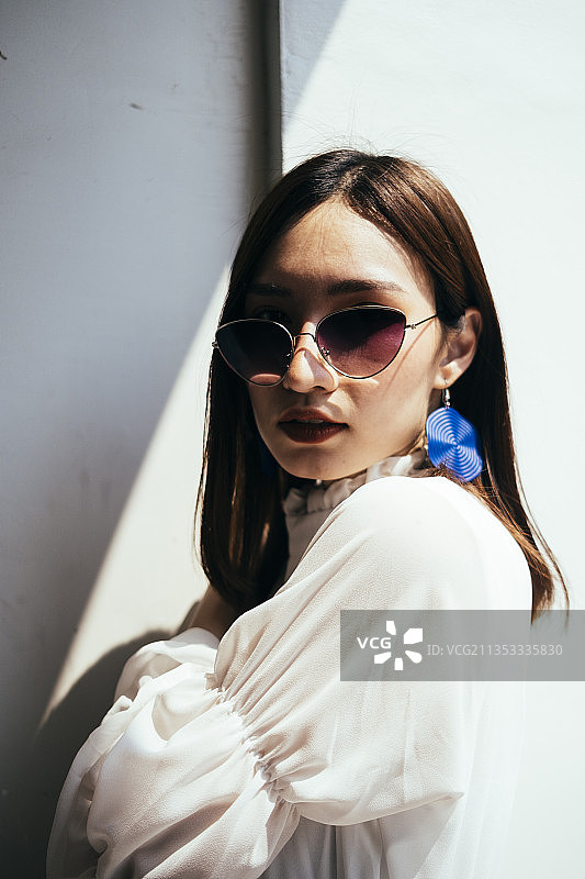 美丽的长发女孩穿着白色的裙子站在阳光和阴影下。图片素材