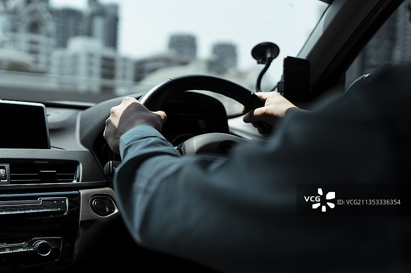 裁剪图像男子手握方向盘紧紧在城市，越过肩膀拍摄。图片素材