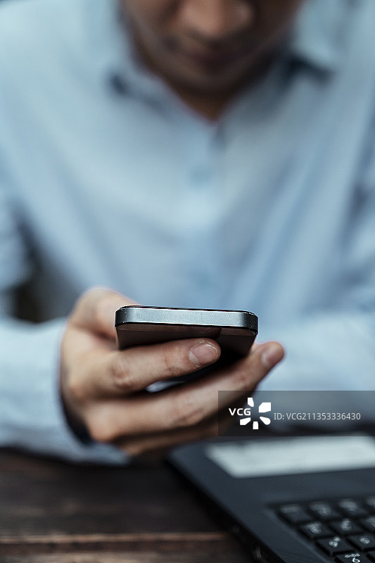 裁剪图像拍摄的智能手机在一个自由职业者的手在蓝色衬衫，垂直。图片素材