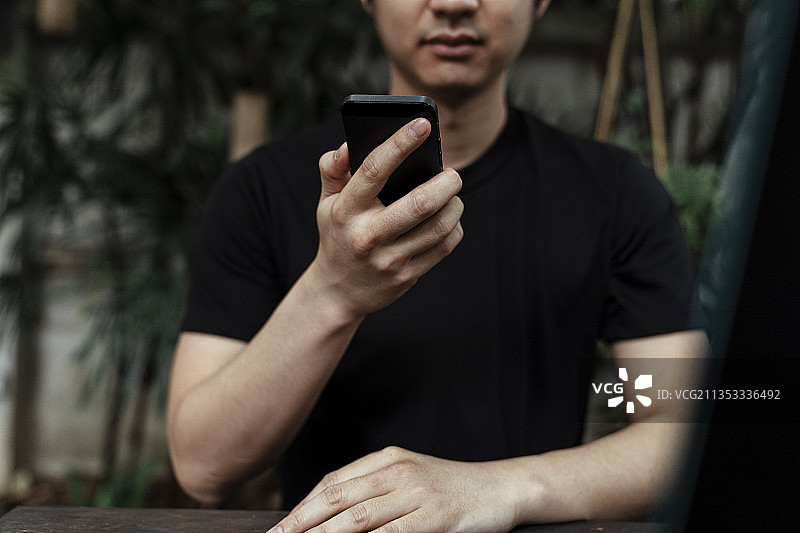 裁剪图像的智能手机在黑人男子手中，而坐在花园里。图片素材