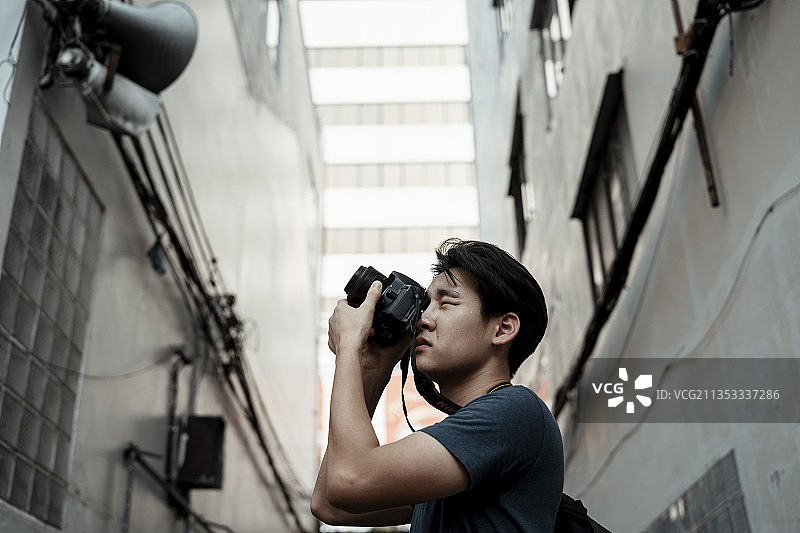 年轻英俊的亚洲摄影师男子拿着相机在城市街道小巷拍照。图片素材