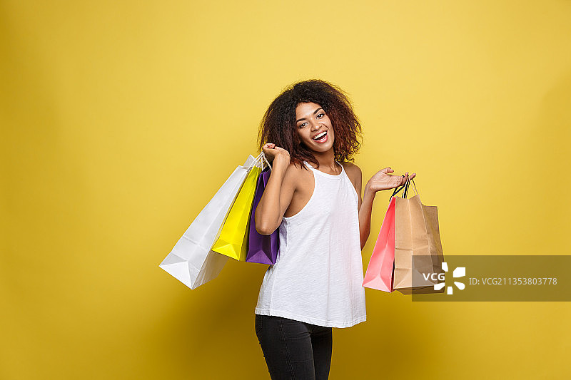 对着黄色背景手提购物袋的微笑女人肖像图片素材