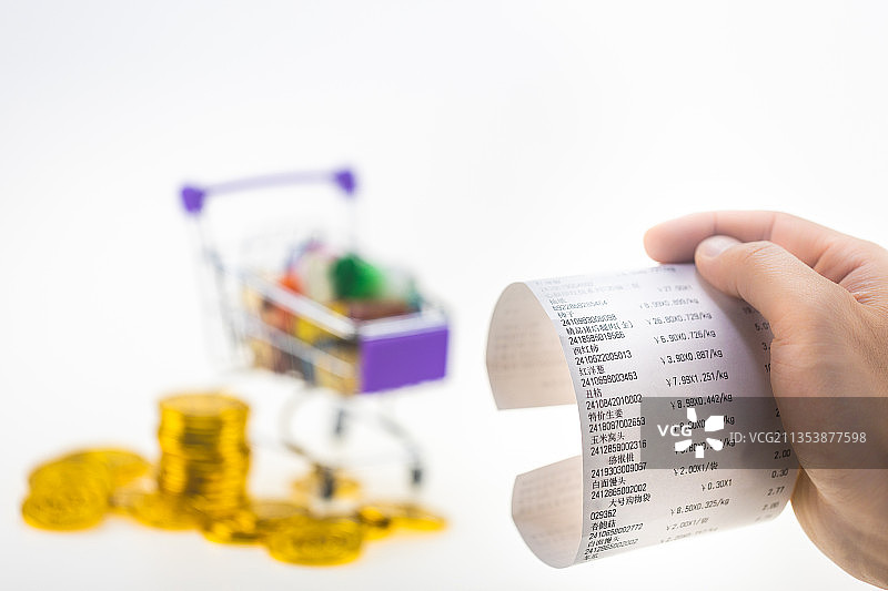 白色背景里的购物车前，男性的手里拿着一张超市小票图片素材