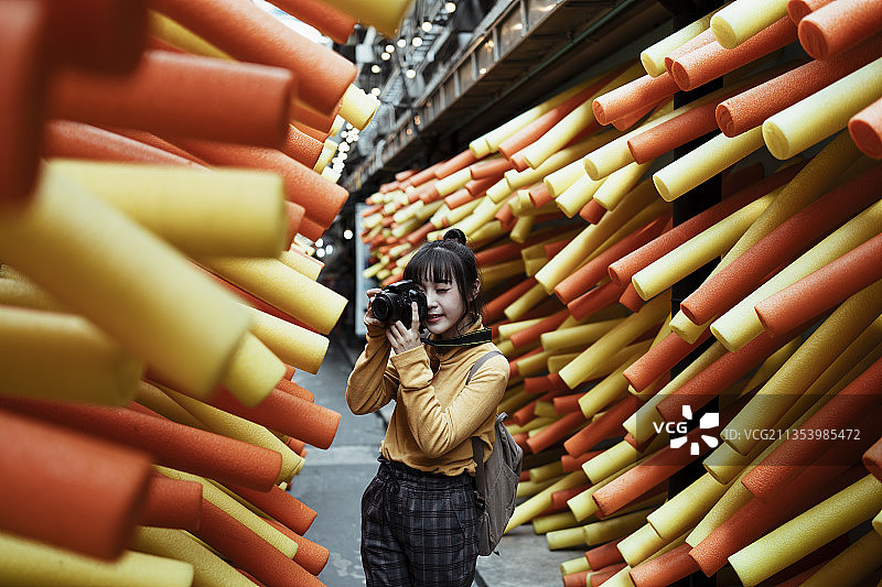 年轻的亚洲妇女穿着黄色毛衣拿着相机在街头巷尾的狂欢节活动拍照。图片素材