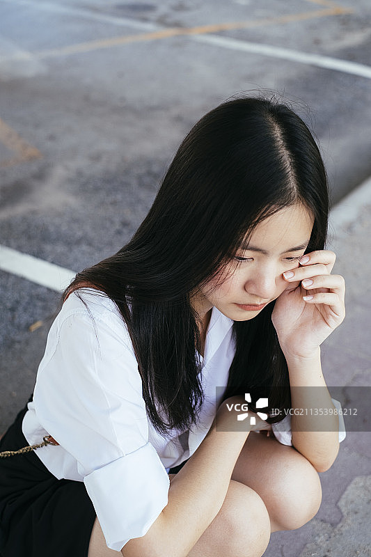 近距离的肖像美丽的长黑发年轻的学生在大学制服哭泣与沮丧的户外。图片素材