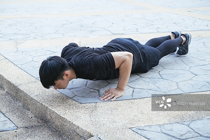 穿着黑色运动服的运动男在地上做俯卧撑。图片素材