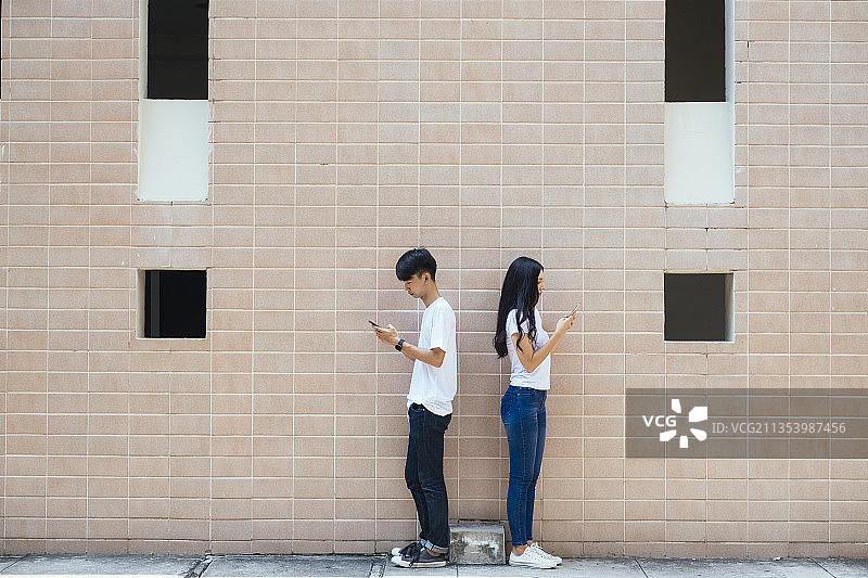 穿着情侣装的情侣站在墙前约会。图片素材