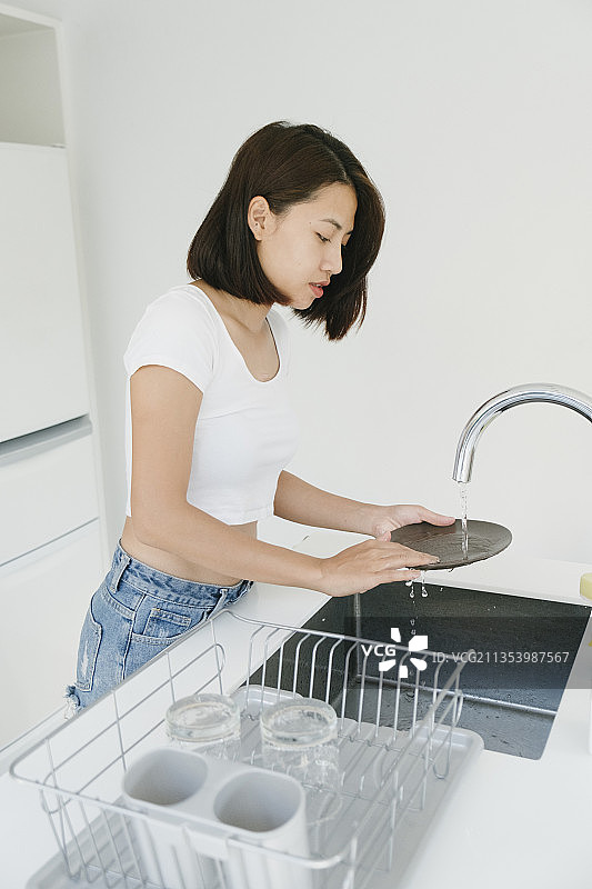 性感的亚洲泰国女人在白色衬衫洗涤在水槽在厨房的盘子。图片素材