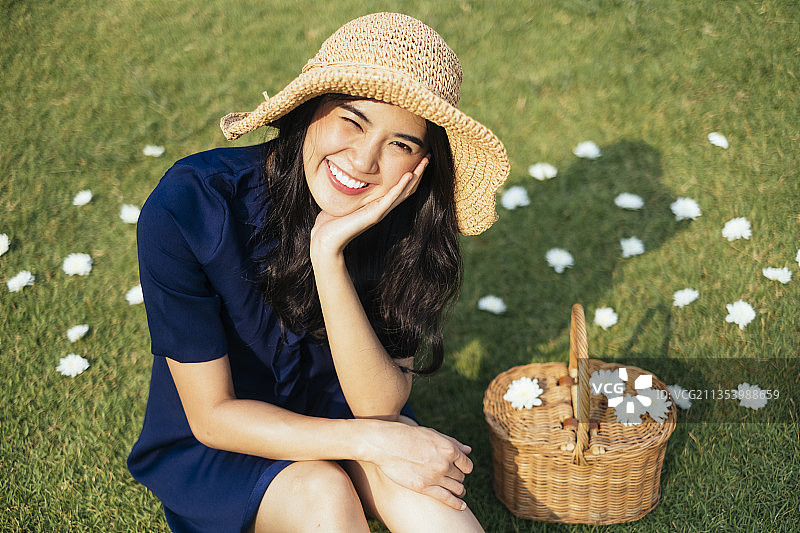 深蓝色的连衣裙女孩微笑着坐在田野里，在强烈的阳光下，白色的花朵之间。图片素材