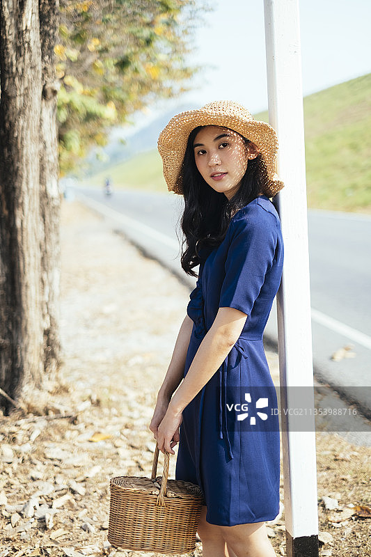 一个泰国女孩拿着篮子站在路边的电线杆旁。图片素材