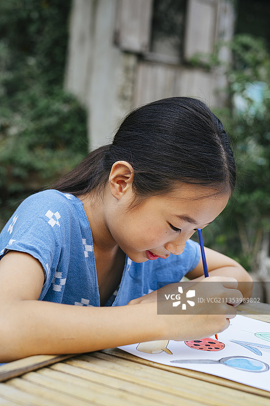 开朗的亚洲小女孩穿着蓝色衬衫在纸上画水彩画。图片素材