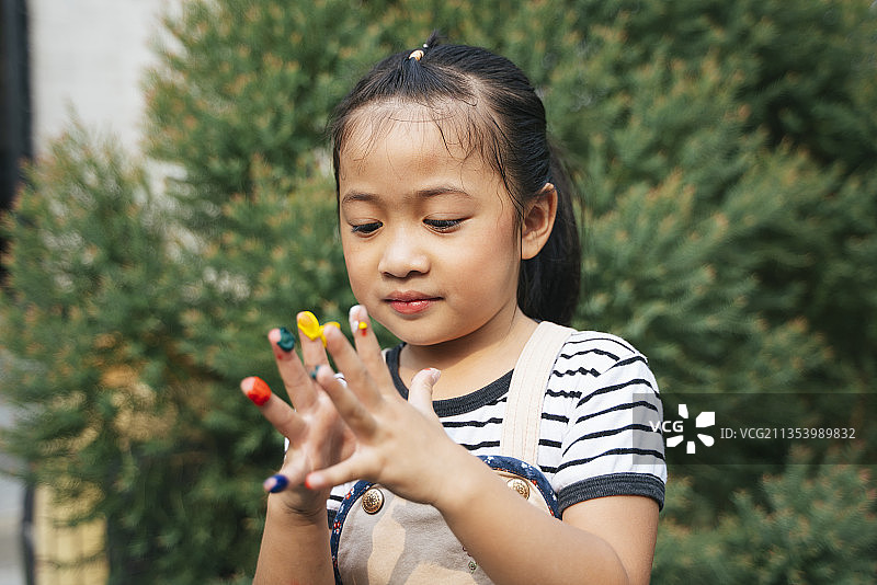 美丽的女孩玩弄手指上的颜色。亚洲女孩的手画在彩色颜料准备手印在花园。图片素材