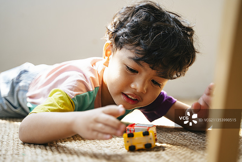 小男孩趴在地板上玩心爱的汽车玩具。图片素材