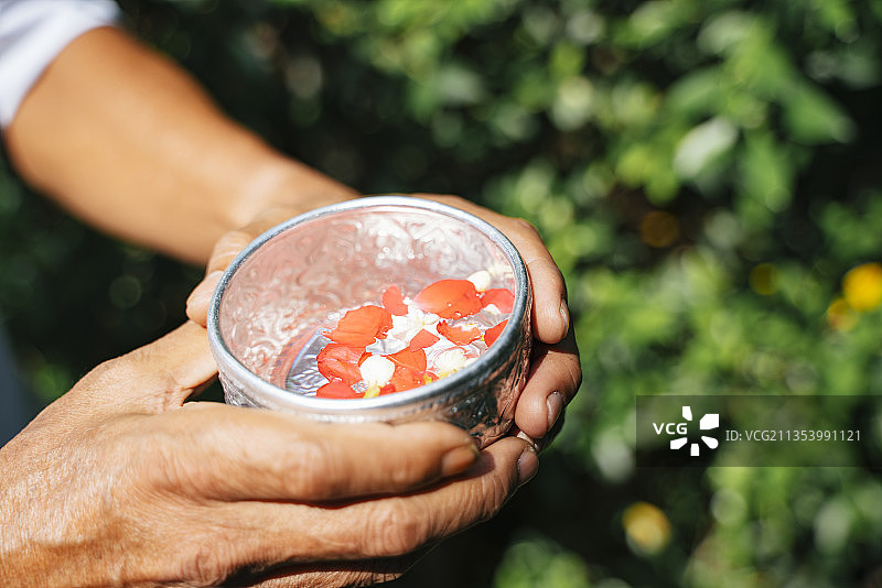 老人双手捧着盛满清水和鲜花的银碗，庆祝泼水节。图片素材