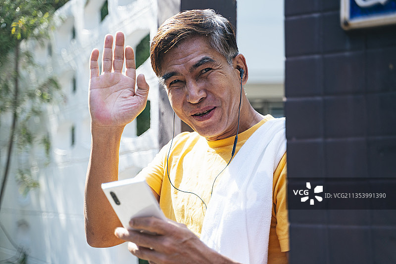 穿着黄色t恤的老人站在他家门前，挥手向邻居打招呼。图片素材