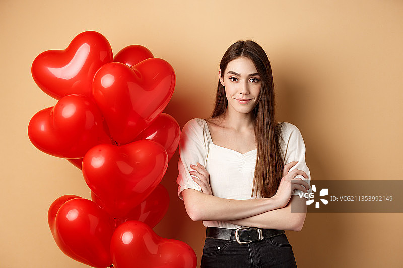 手持红色心形氦气球的年轻女子人像，米色背景图片素材