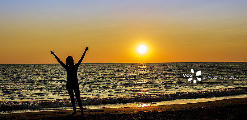 日落时分在海滩上眺望天空的女子剪影，意大利利沃诺省滨海迪比博纳图片素材