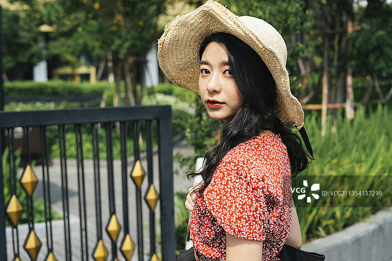 年轻美丽的泰国亚洲女旅行者穿着红色的裙子和帽子在曼谷城市公园旅游。图片素材