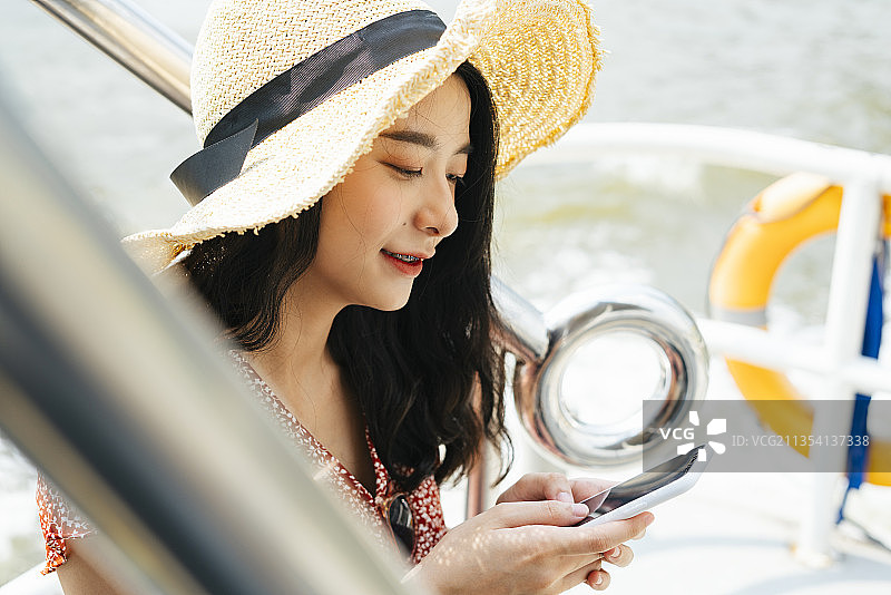 开朗年轻美丽的泰国亚洲旅行者女人穿着红色的衣服和帽子在河码头使用智能手机。图片素材