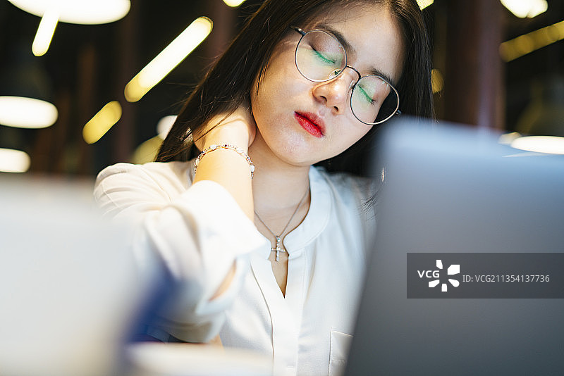 疲惫紧张的亚洲女人戴着眼镜坐在电脑笔记本电脑前。加班。疲惫和疲劳。图片素材