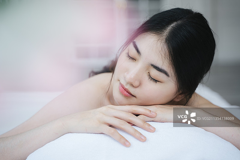 长发女孩在白色毛巾躺在白色的床上，在水疗中心享受泰式按摩放松。图片素材