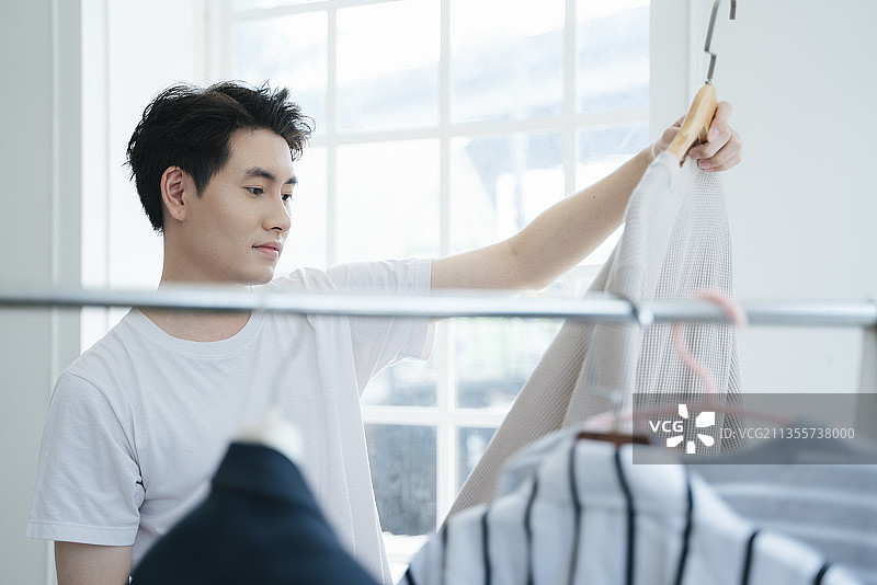 一个男人选择出门穿的衣服，然后决定哪一件更好。图片素材