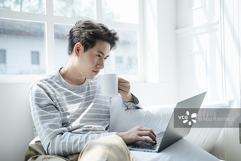 一个男人在家工作，在窗口喝热咖啡。图片素材