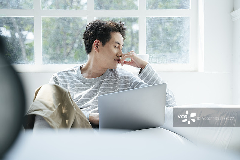 一个男人在家工作，在窗口喝热咖啡。图片素材